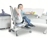 Uśmiechnięty chłopiec siedzi przy biurku na ergonomicznym krześle, czytając książkę.