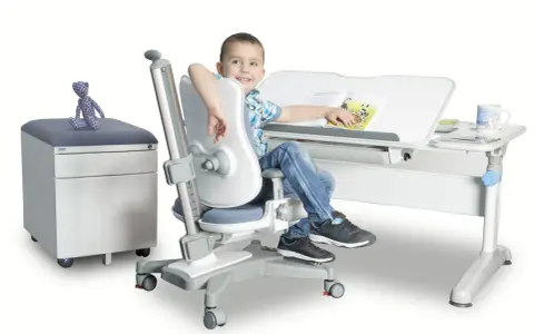 Uśmiechnięty chłopiec siedzi przy biurku na ergonomicznym krześle, czytając książkę.